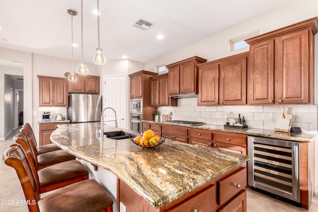 kitchen with appliances with stainless steel finishes, beverage cooler, light stone countertops, and an island with sink