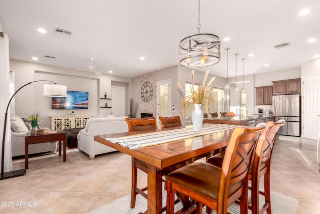 dining area featuring ceiling fan with notable chandelier, sink, light tile patterned floors, and a large fireplace