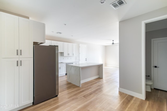 kitchen with white cabinets, a kitchen island, stainless steel appliances, ceiling fan, and light hardwood / wood-style flooring