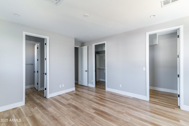 unfurnished bedroom featuring light hardwood / wood-style floors, ensuite bath, a closet, and a walk in closet