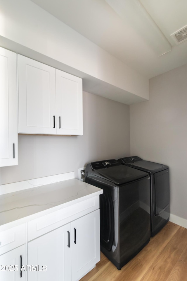 laundry room with washing machine and dryer, light hardwood / wood-style flooring, and cabinets