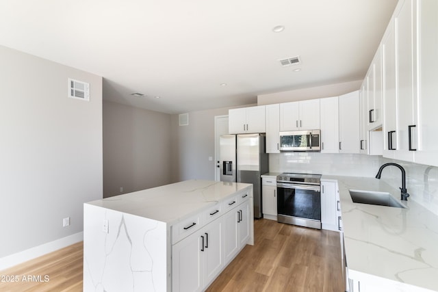 kitchen with white cabinets, a center island, light stone countertops, and appliances with stainless steel finishes