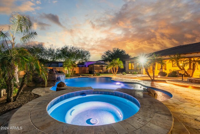 pool at dusk featuring a patio area and an in ground hot tub