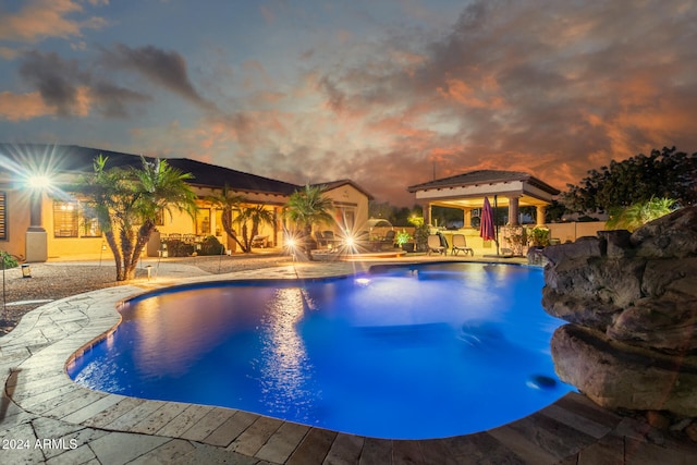 pool at dusk with a patio area and pool water feature