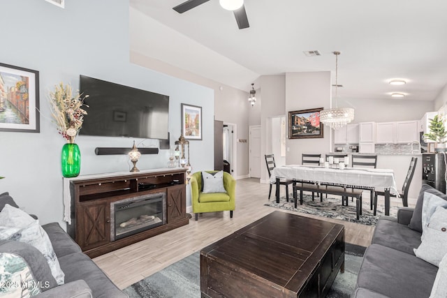 living room featuring ceiling fan with notable chandelier, light hardwood / wood-style floors, and vaulted ceiling