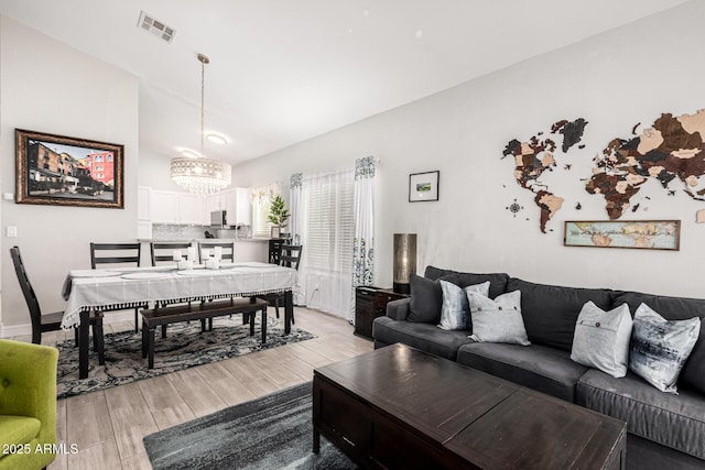 living room featuring light wood-type flooring, vaulted ceiling, and a notable chandelier