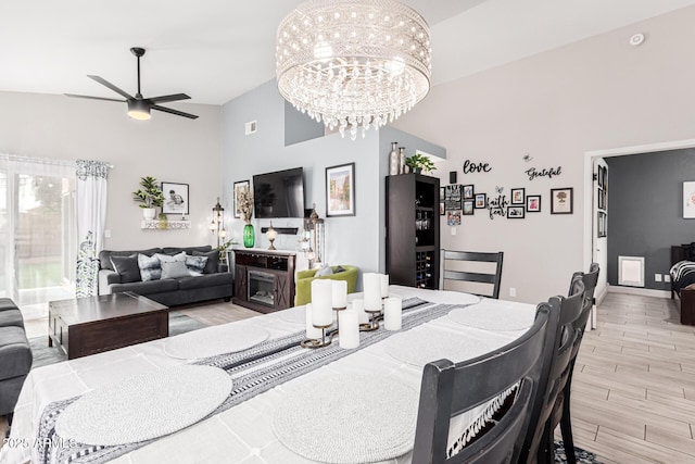 dining space with light wood-type flooring, vaulted ceiling, a fireplace, and ceiling fan with notable chandelier