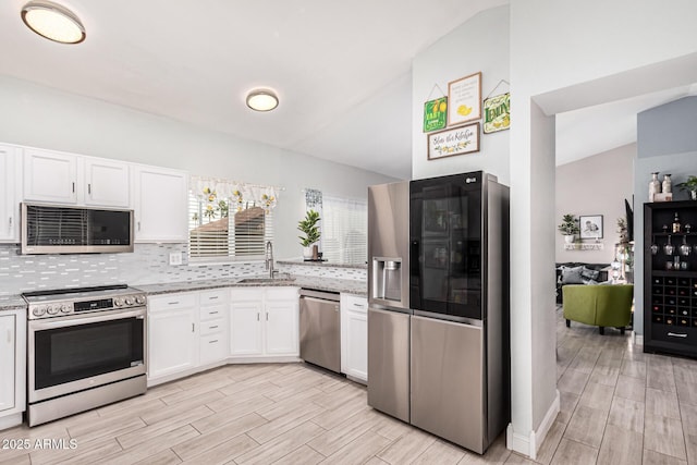 kitchen with light stone countertops, sink, backsplash, appliances with stainless steel finishes, and white cabinets