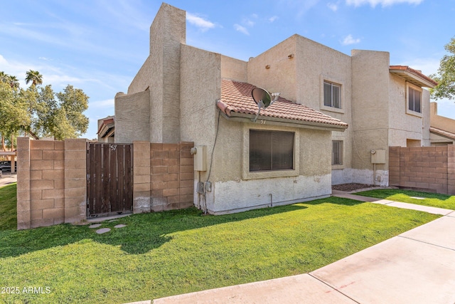 view of front of house featuring a tile roof, stucco siding, a gate, fence, and a front lawn