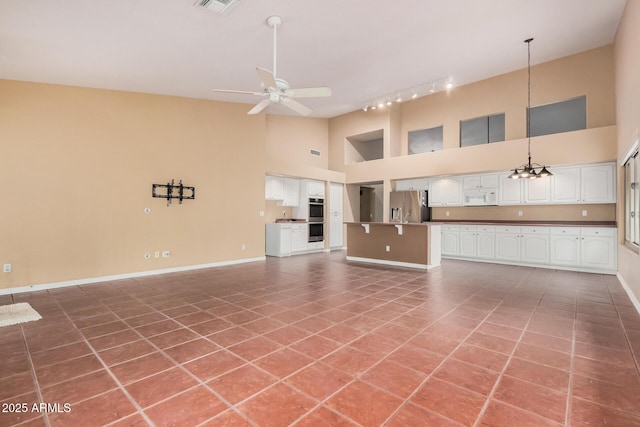 unfurnished living room with tile patterned flooring, rail lighting, ceiling fan with notable chandelier, and high vaulted ceiling