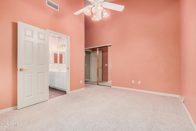 unfurnished bedroom with ceiling fan, a towering ceiling, ensuite bathroom, and light carpet