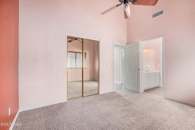 unfurnished bedroom with ceiling fan, a high ceiling, connected bathroom, light colored carpet, and a closet