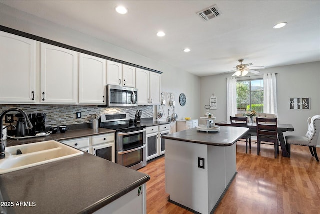 kitchen featuring stainless steel appliances, visible vents, a sink, and dark countertops