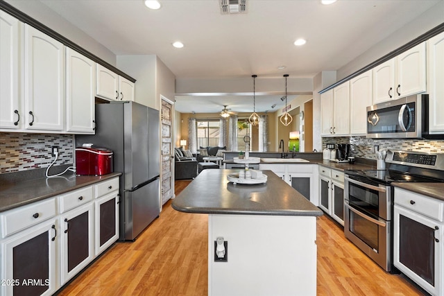 kitchen featuring a peninsula, a center island, a sink, dark countertops, and stainless steel appliances