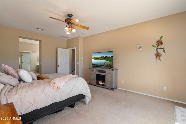 bedroom featuring visible vents, baseboards, ceiling fan, a lit fireplace, and light carpet