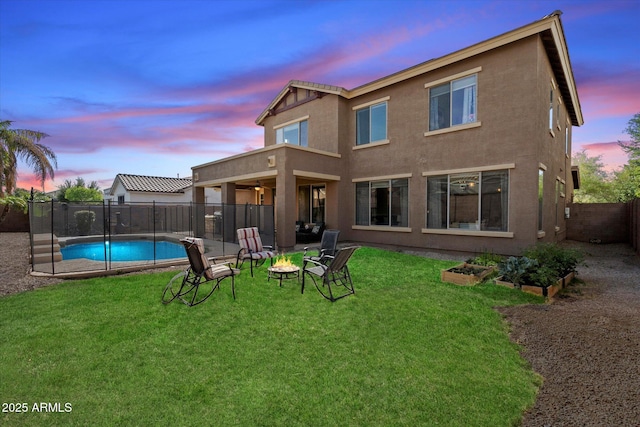 back of house at dusk featuring a vegetable garden, a yard, a fenced backyard, stucco siding, and a fenced in pool