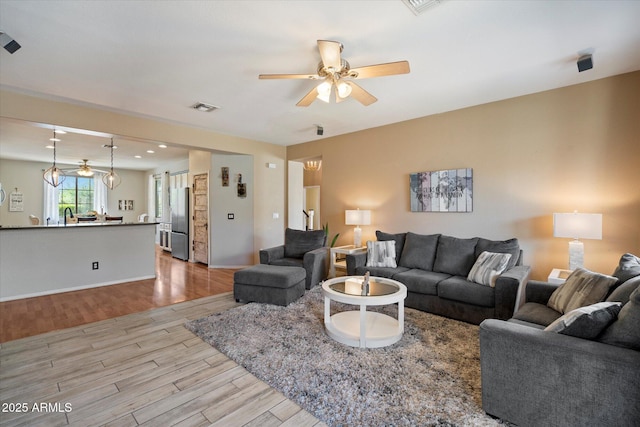 living room featuring light wood-style floors, baseboards, visible vents, and ceiling fan