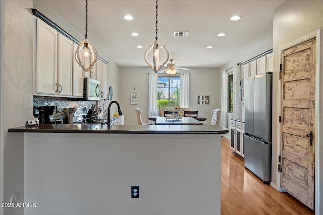 kitchen with a peninsula, appliances with stainless steel finishes, light wood finished floors, and recessed lighting