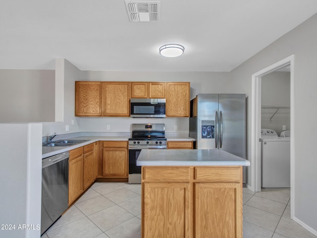 kitchen with sink, a kitchen island, appliances with stainless steel finishes, light tile patterned floors, and separate washer and dryer