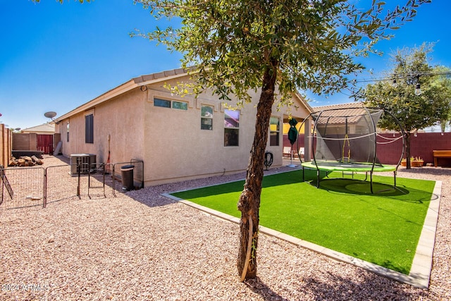 back of house featuring central AC unit, a lawn, and a trampoline