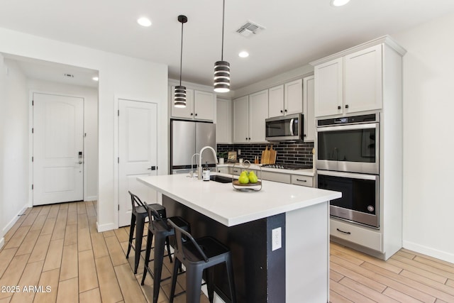 6641 N Desert Shadow Ln, Phoenix, AZ 85014 - kitchen with appliances with stainless steel finishes, light wood-type flooring, decorative backsplash, a center island with sink, and a kitchen breakfast bar