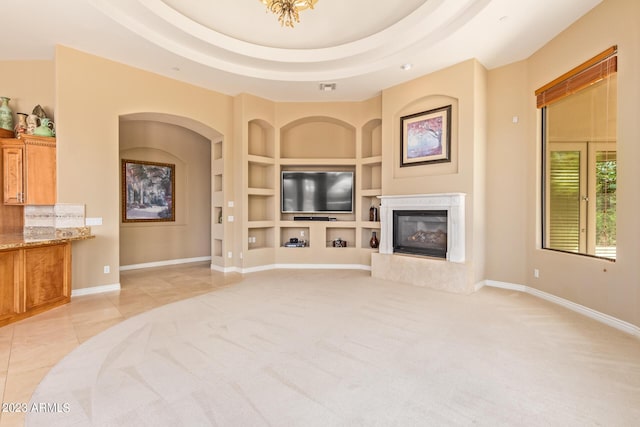 carpeted living room with a high end fireplace, built in features, and a raised ceiling