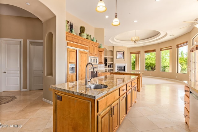 kitchen featuring pendant lighting, sink, a raised ceiling, light tile patterned floors, and a center island with sink