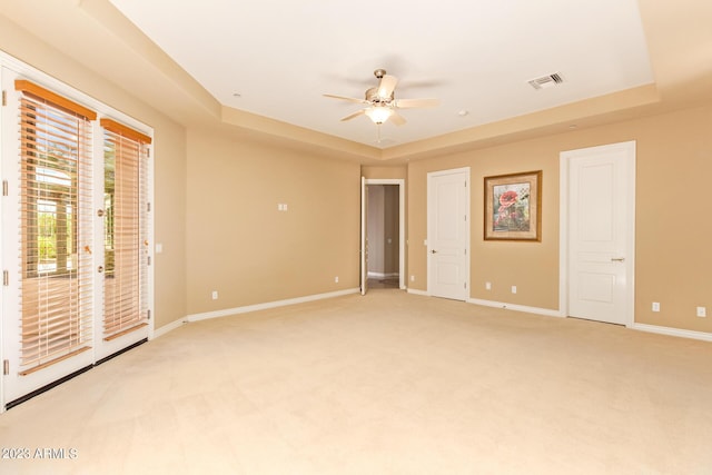 carpeted empty room with ceiling fan and a raised ceiling