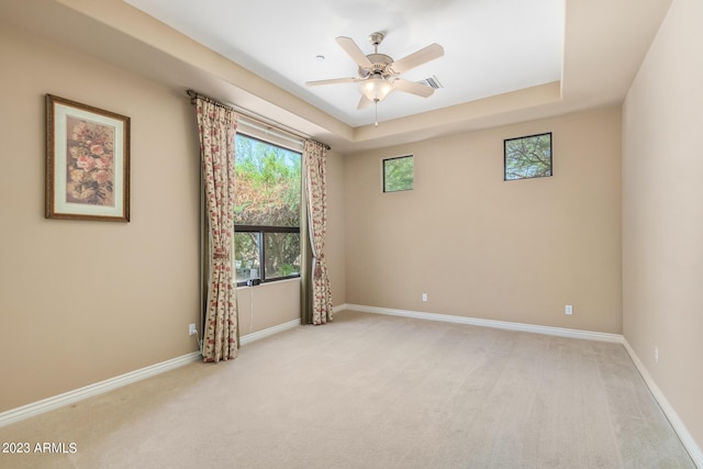 empty room with ceiling fan, light carpet, and a tray ceiling