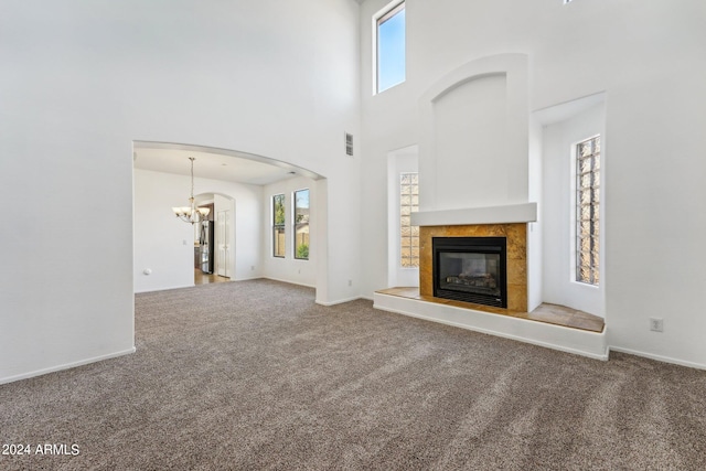 unfurnished living room featuring carpet floors, a tiled fireplace, a high ceiling, and a chandelier