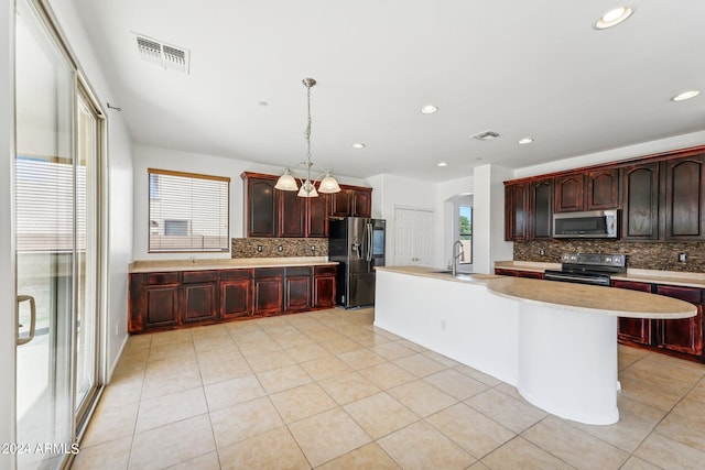 kitchen featuring appliances with stainless steel finishes, a wealth of natural light, decorative light fixtures, and an island with sink