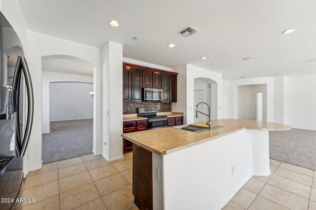 kitchen featuring light carpet, a kitchen island with sink, and stainless steel appliances