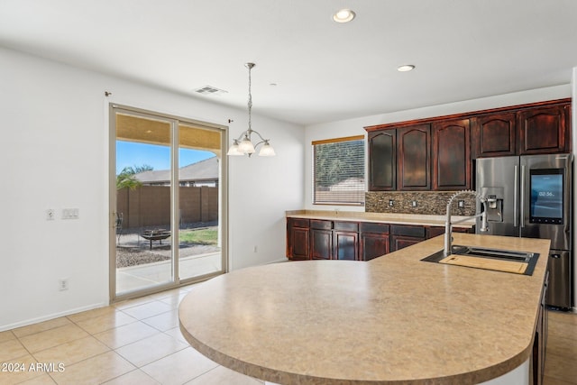 kitchen featuring pendant lighting, stainless steel fridge, sink, a center island with sink, and an inviting chandelier