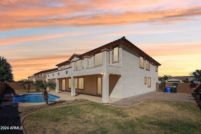 back house at dusk featuring a yard, a fenced in pool, a balcony, and a patio area