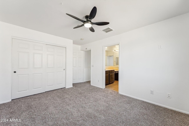 unfurnished bedroom with ceiling fan, a closet, light carpet, and ensuite bath