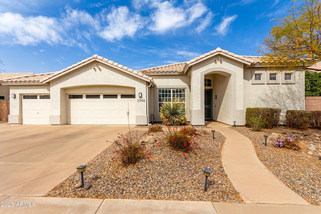 mediterranean / spanish-style home with a garage, a tile roof, driveway, and stucco siding