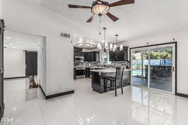 4020 W Anderson Dr, Glendale, AZ 85308 - kitchen featuring appliances with stainless steel finishes, dark cabinetry, a textured ceiling, lofted ceiling, and a barn door