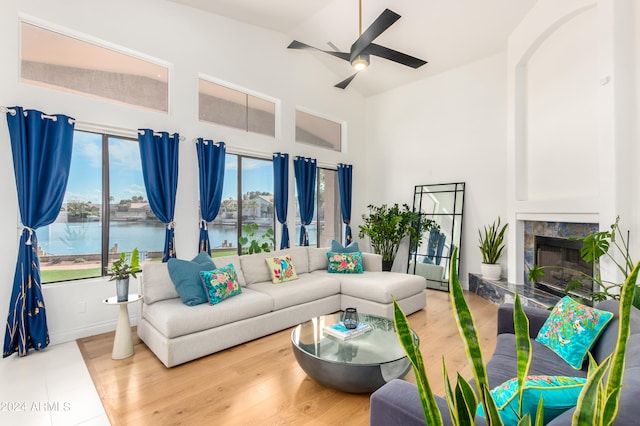 living room with ceiling fan, a water view, light hardwood / wood-style flooring, and a premium fireplace