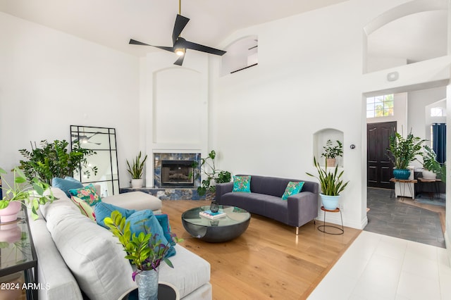 living room with ceiling fan, a high end fireplace, light hardwood / wood-style floors, and a towering ceiling