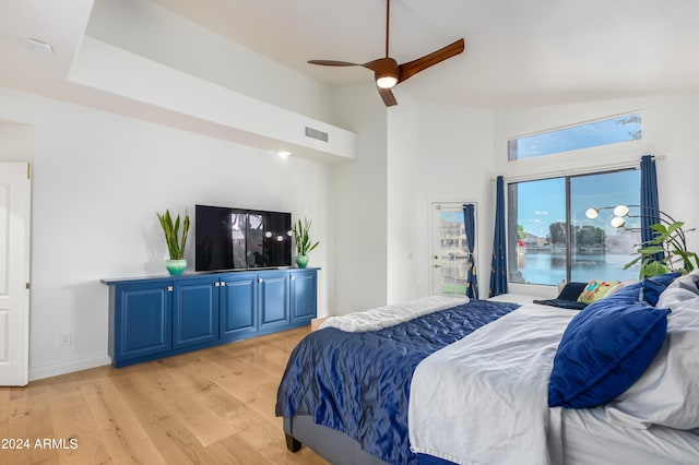 bedroom featuring ceiling fan, a water view, light wood-type flooring, and high vaulted ceiling