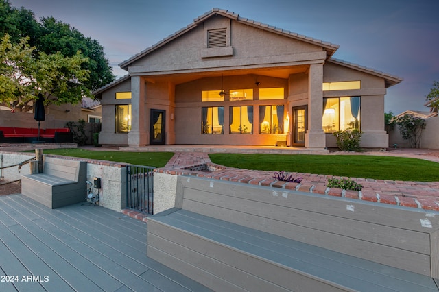 back house at dusk with a wooden deck and a lawn