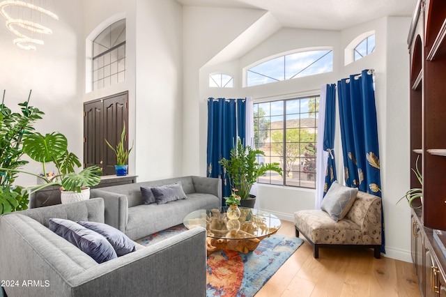 living room with high vaulted ceiling, an inviting chandelier, and light hardwood / wood-style flooring