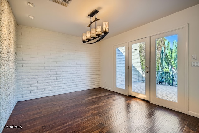 unfurnished dining area with french doors, dark hardwood / wood-style floors, an inviting chandelier, and brick wall