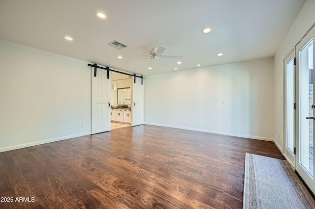 spare room featuring a barn door, ceiling fan, dark hardwood / wood-style flooring, and plenty of natural light