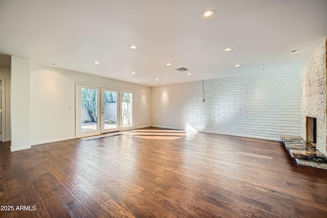 unfurnished living room featuring a fireplace, dark wood-type flooring, and brick wall