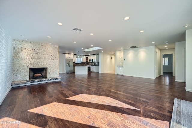 unfurnished living room with a stone fireplace and dark wood-type flooring