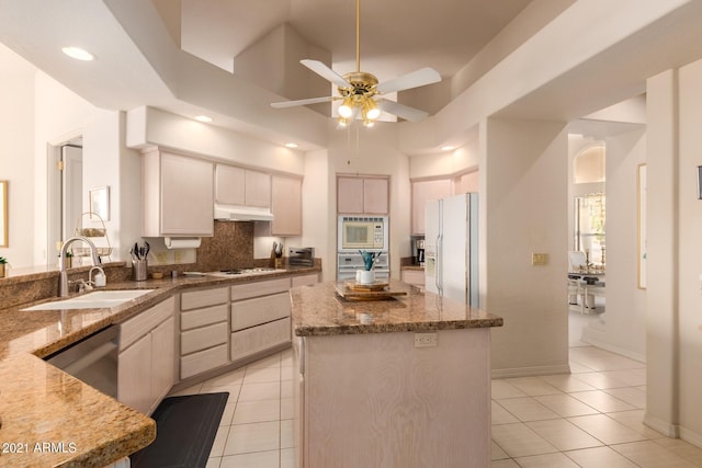 kitchen with white appliances, a sink, light stone counters, and under cabinet range hood