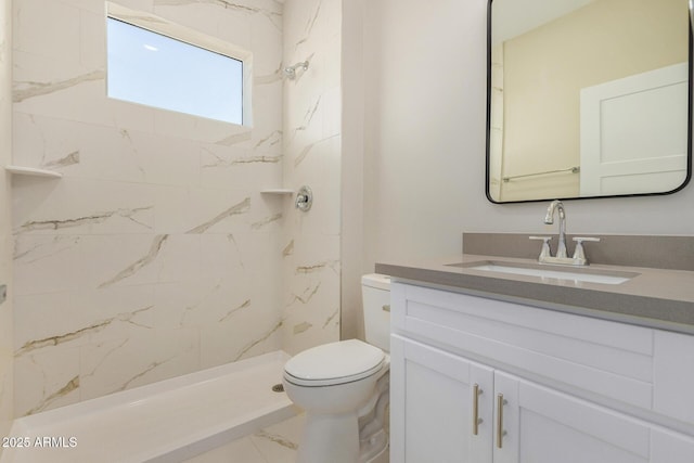 bathroom featuring a tile shower, vanity, and toilet