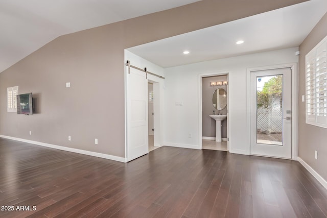 interior space featuring lofted ceiling, a barn door, baseboards, and dark wood finished floors