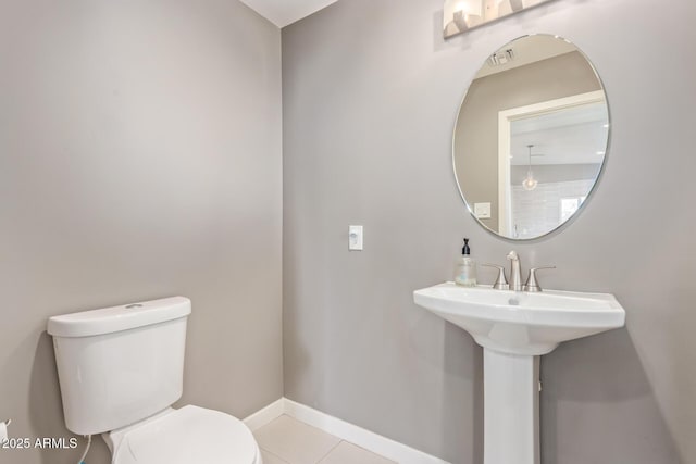 half bath with visible vents, toilet, a sink, tile patterned flooring, and baseboards